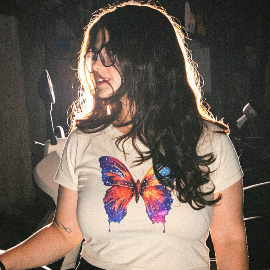 Person wearing a white t-shirt with a colorful butterfly design in a dark setting.