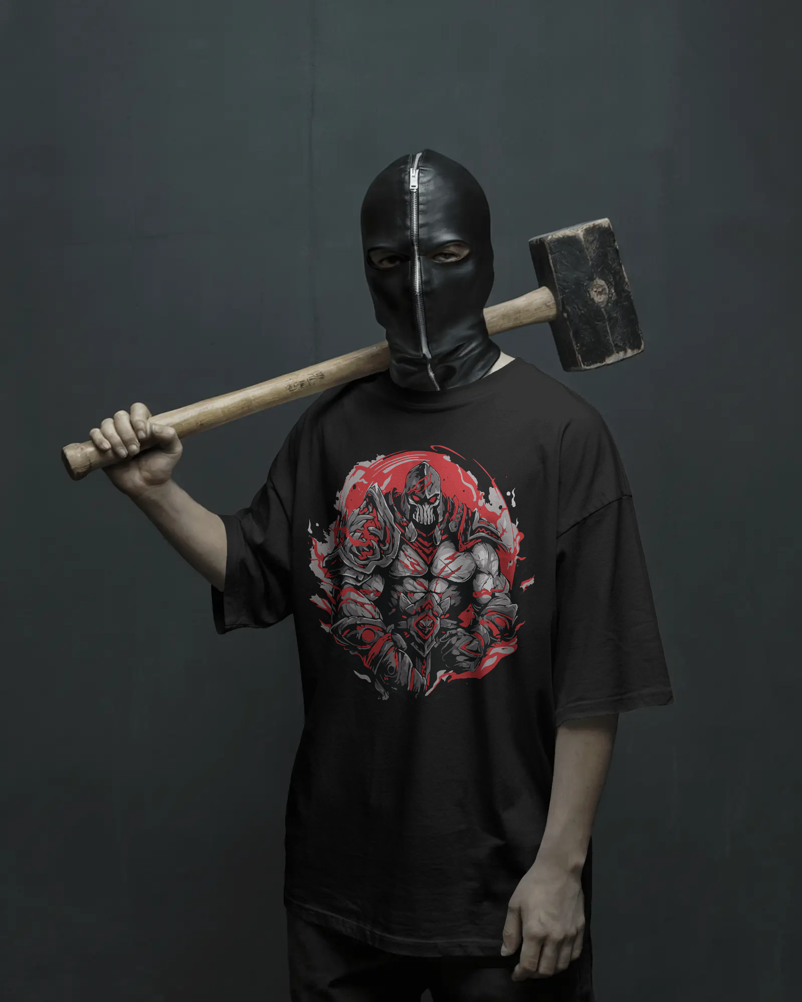 A person wearing a black oversized t-shirt featuring a red armored warrior graphic, standing confidently against a dark background holding a large hammer over the shoulder. The look is bold and streetwear-inspired.