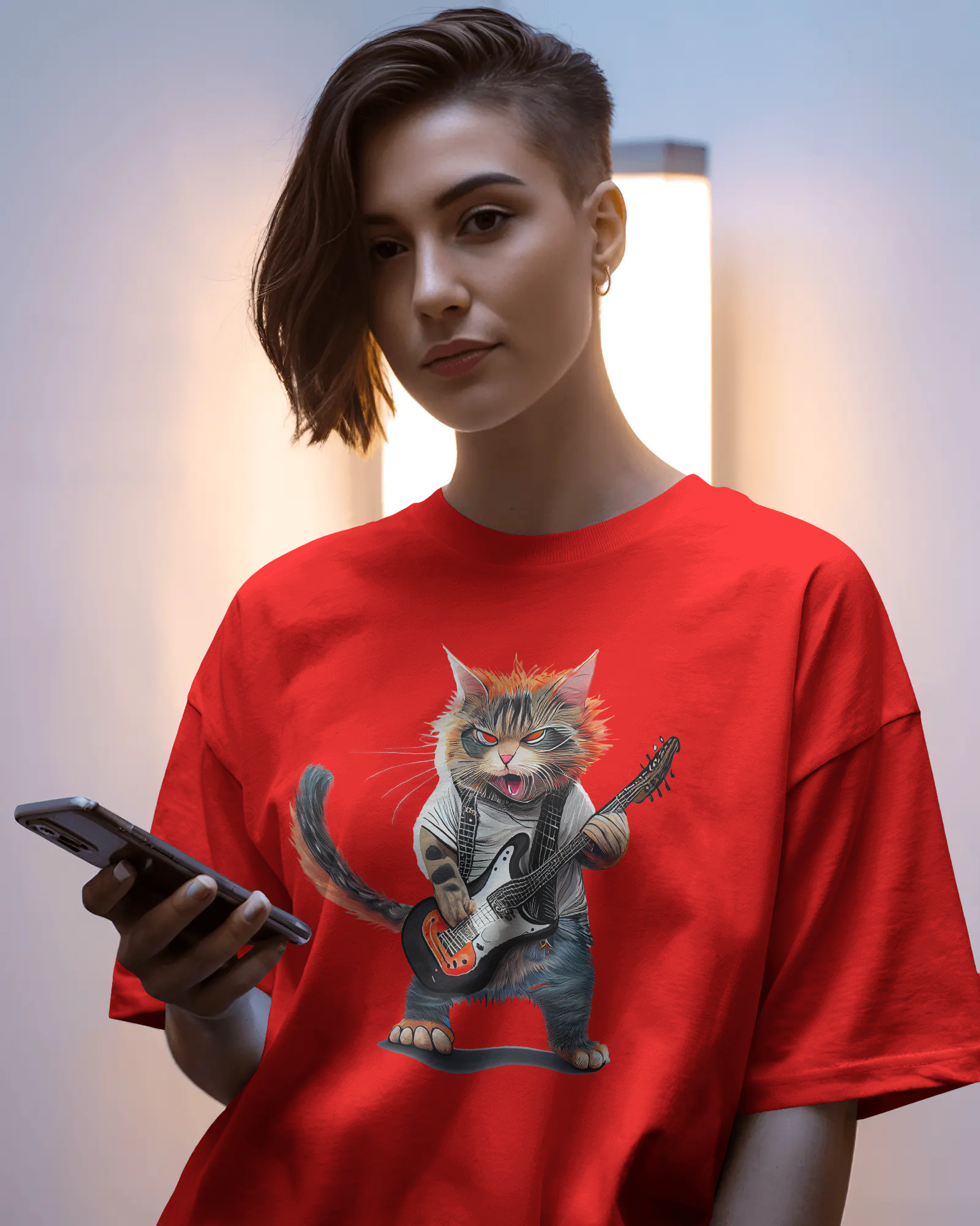 red oversized T-shirt featuring a rockstar cat graphic holding a guitar, standing in a studio with vibrant blue and green lighting.