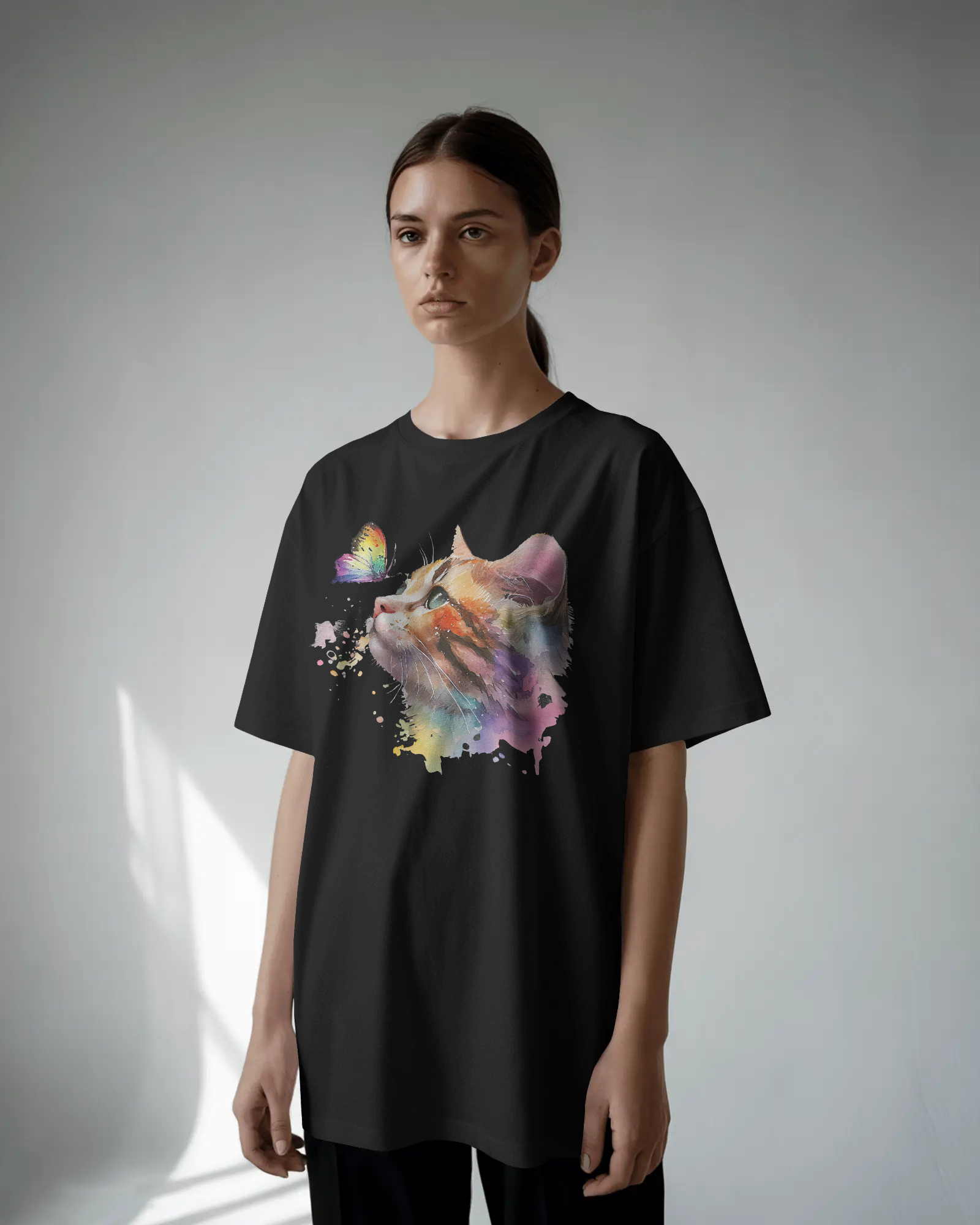 Person wearing a black t-shirt with a colorful cat graphic on a plain background