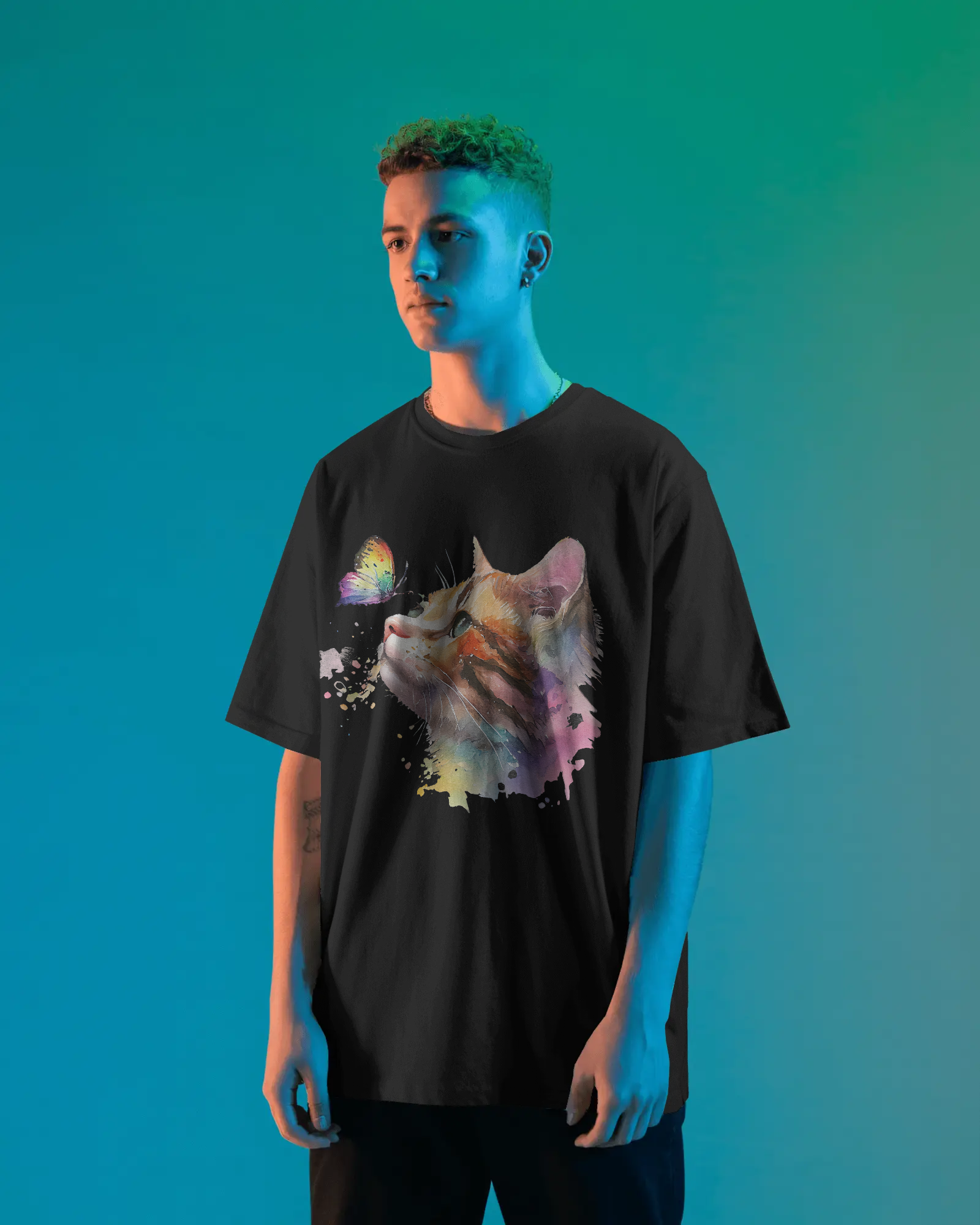 A person wearing a red oversized T-shirt featuring a colorful watercolor cat looking at a butterfly, standing in a studio with blue-green lighting.