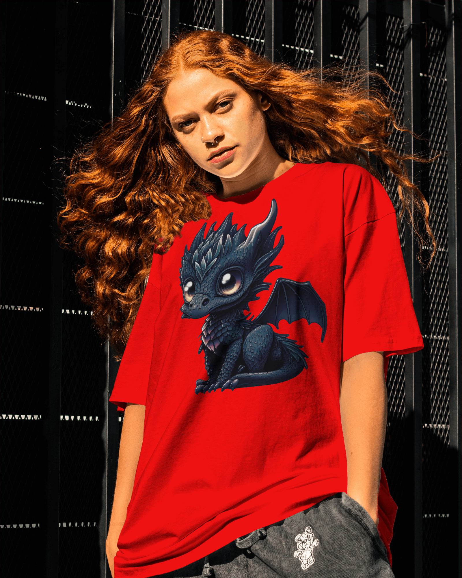 A woman wearing a red oversized T-shirt featuring a cute fantasy baby dragon graphic, standing in an urban setting with dramatic lighting.