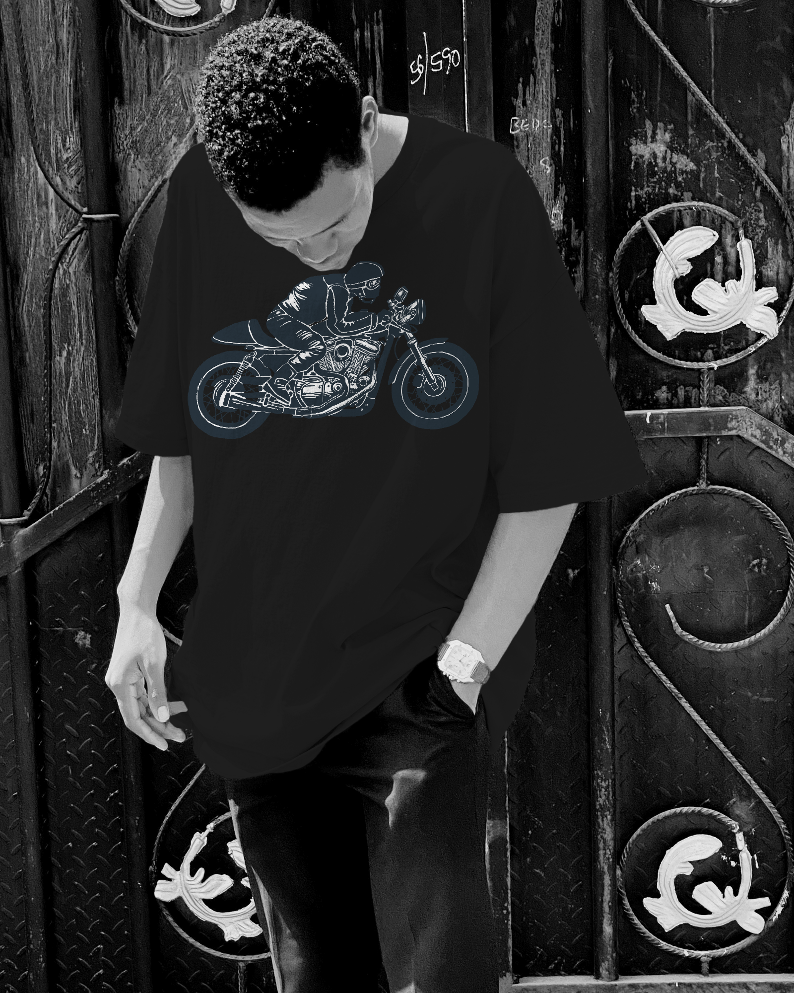Person wearing a black t-shirt with a graphic design of a motorcycle in front of a decorative metal door.