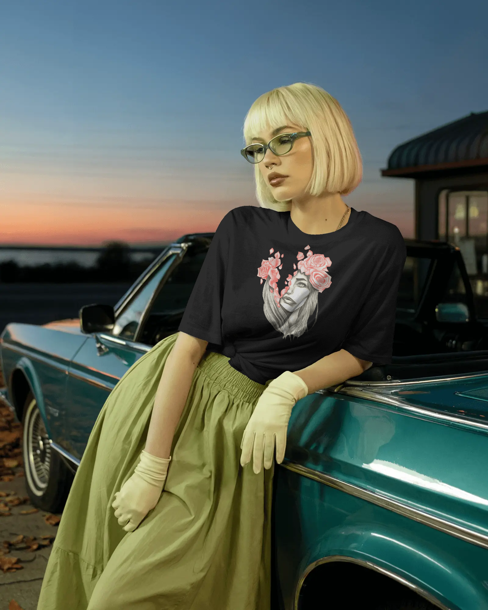 Person wearing a black t-shirt with a graphic design, green skirt, and white gloves leaning against a vintage car at sunset.