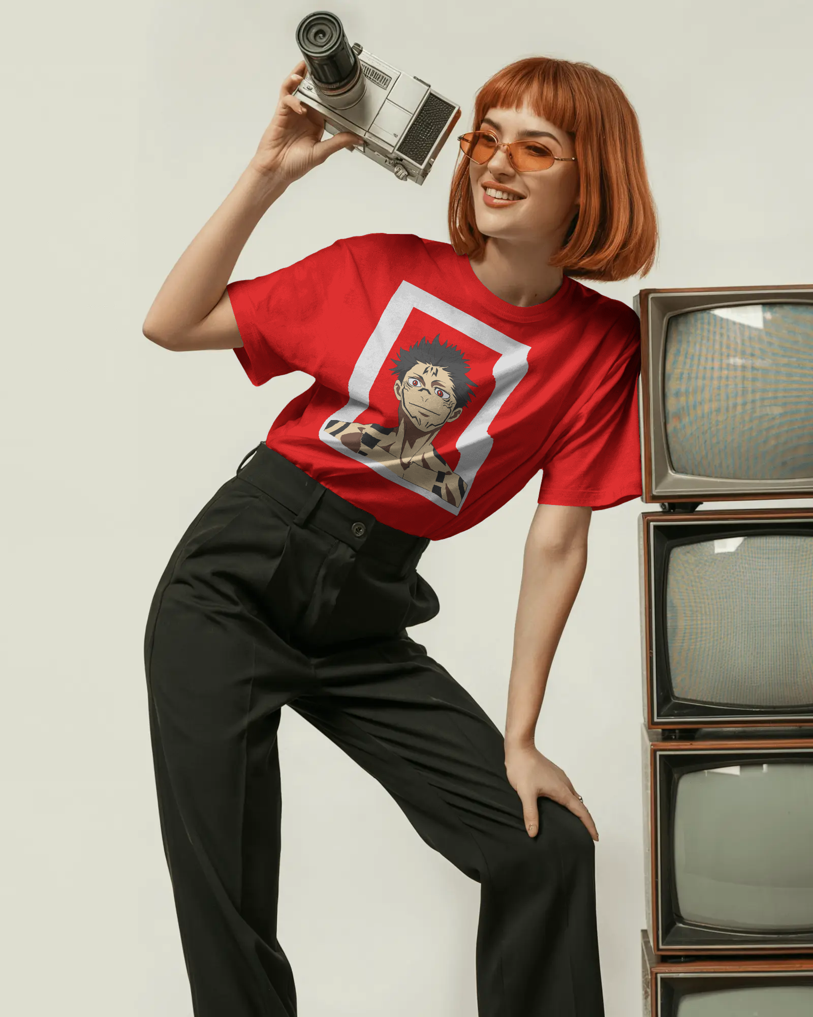 Person wearing a red t-shirt with a graphic design, holding a camera, standing next to vintage TVs.