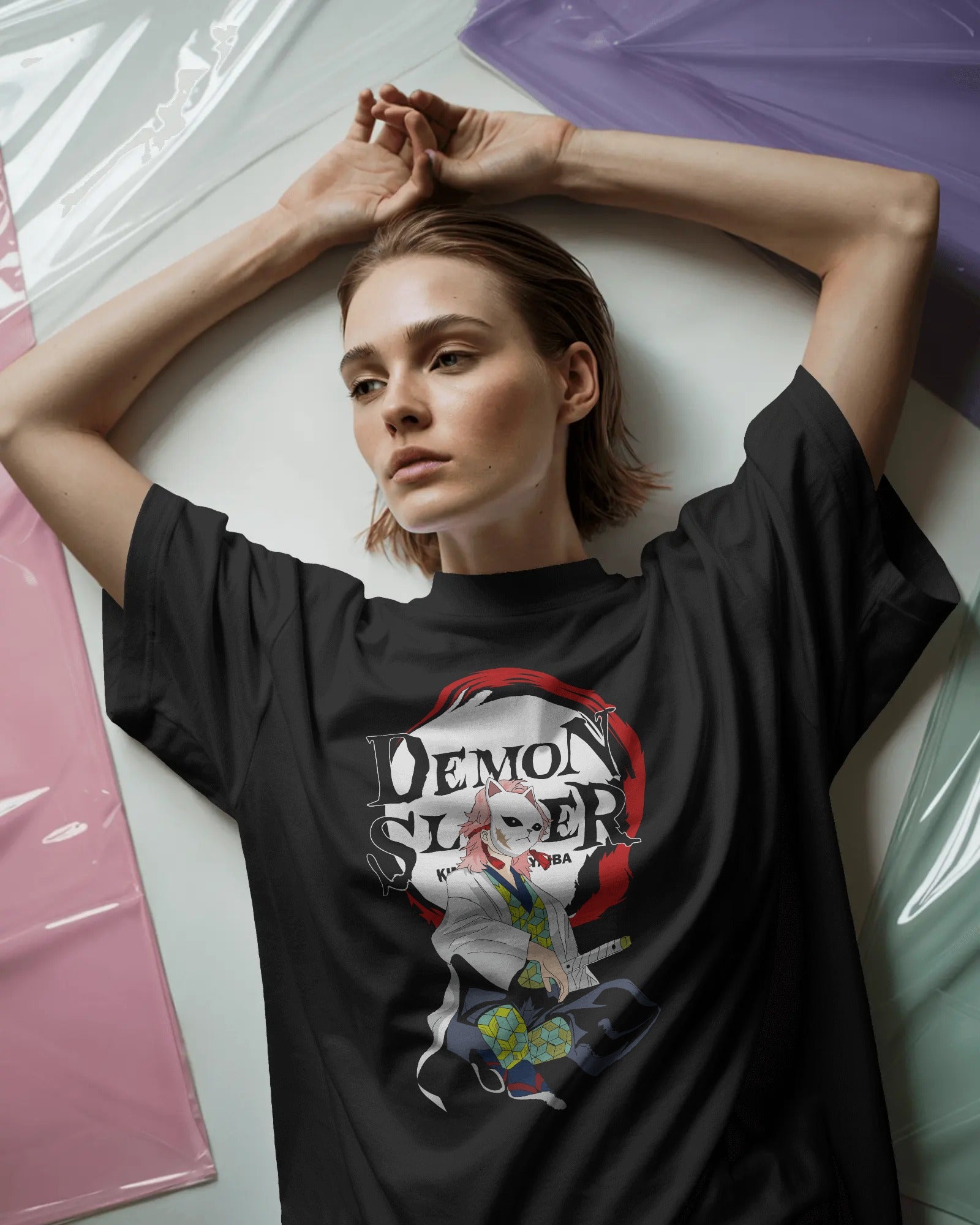 Person wearing a black t-shirt with 'Demon Slayer' graphic design, lying on a white surface.