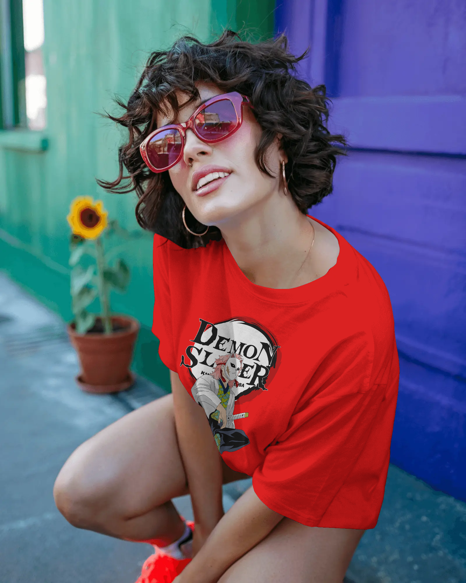 Woman wearing a red t-shirt with a graphic design, sitting against a colorful wall.