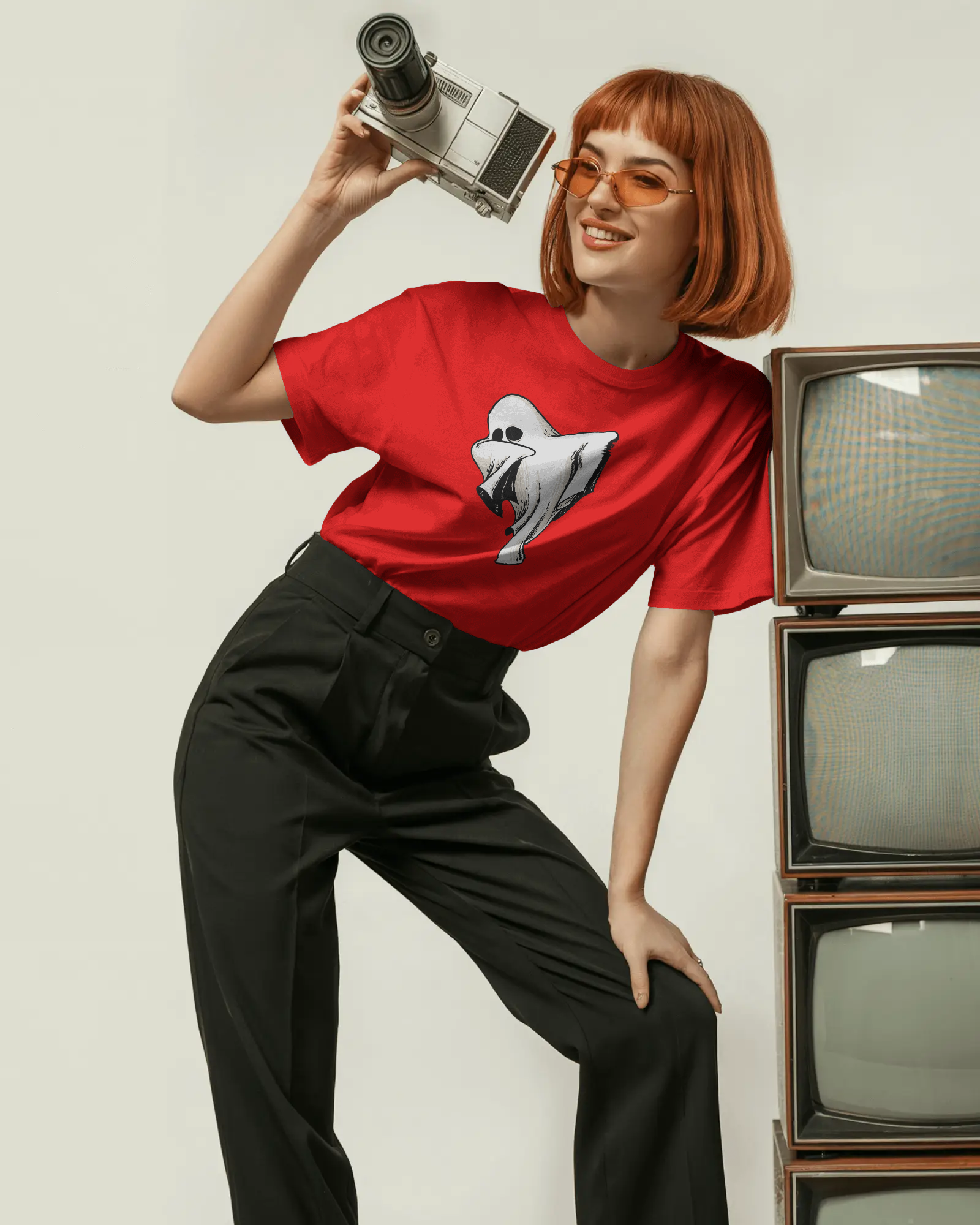 Person wearing a red t-shirt with a graphic design, holding a camera, standing next to vintage TVs.