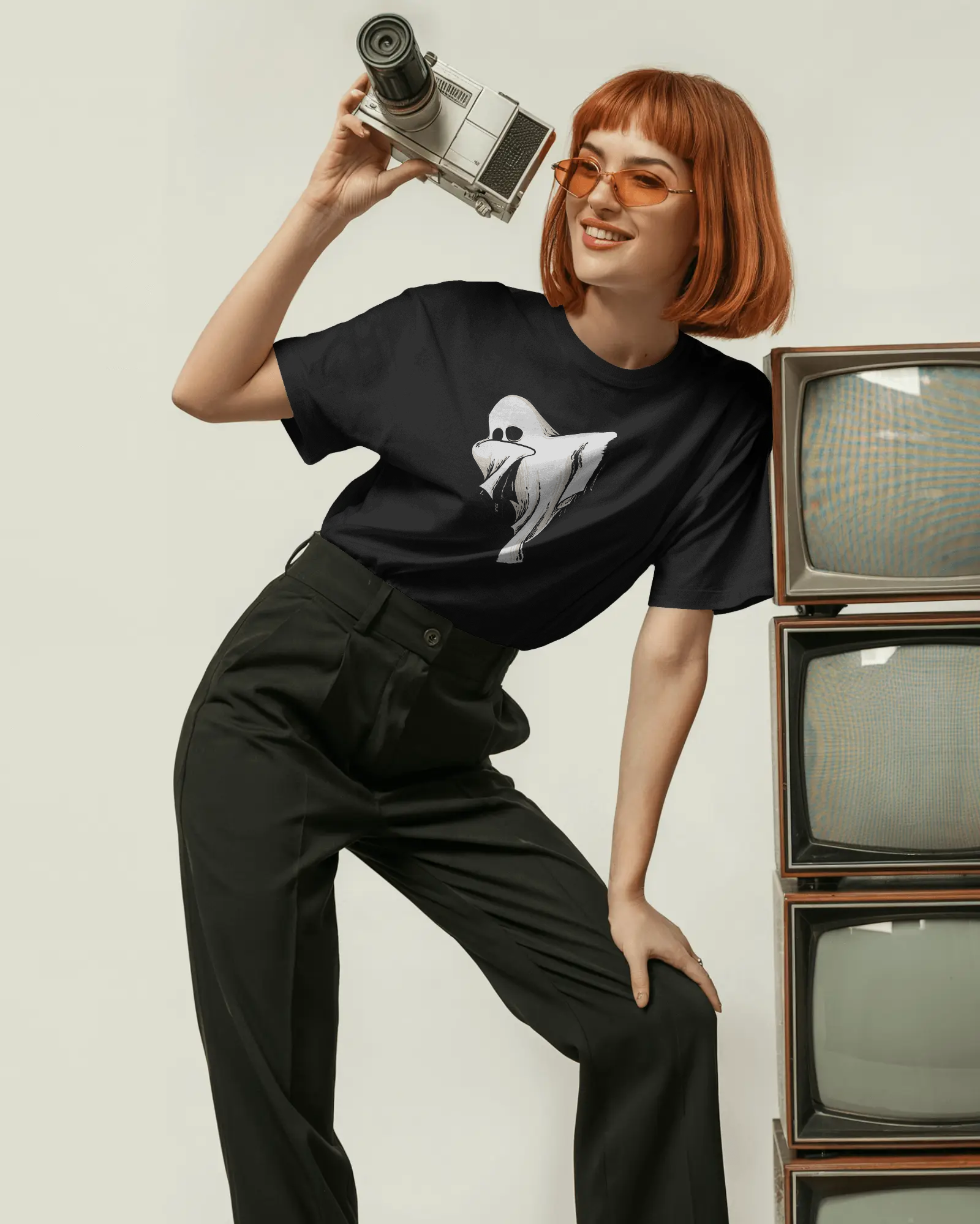 Person wearing a black t-shirt with a graphic design, holding a camera, standing next to vintage TVs.