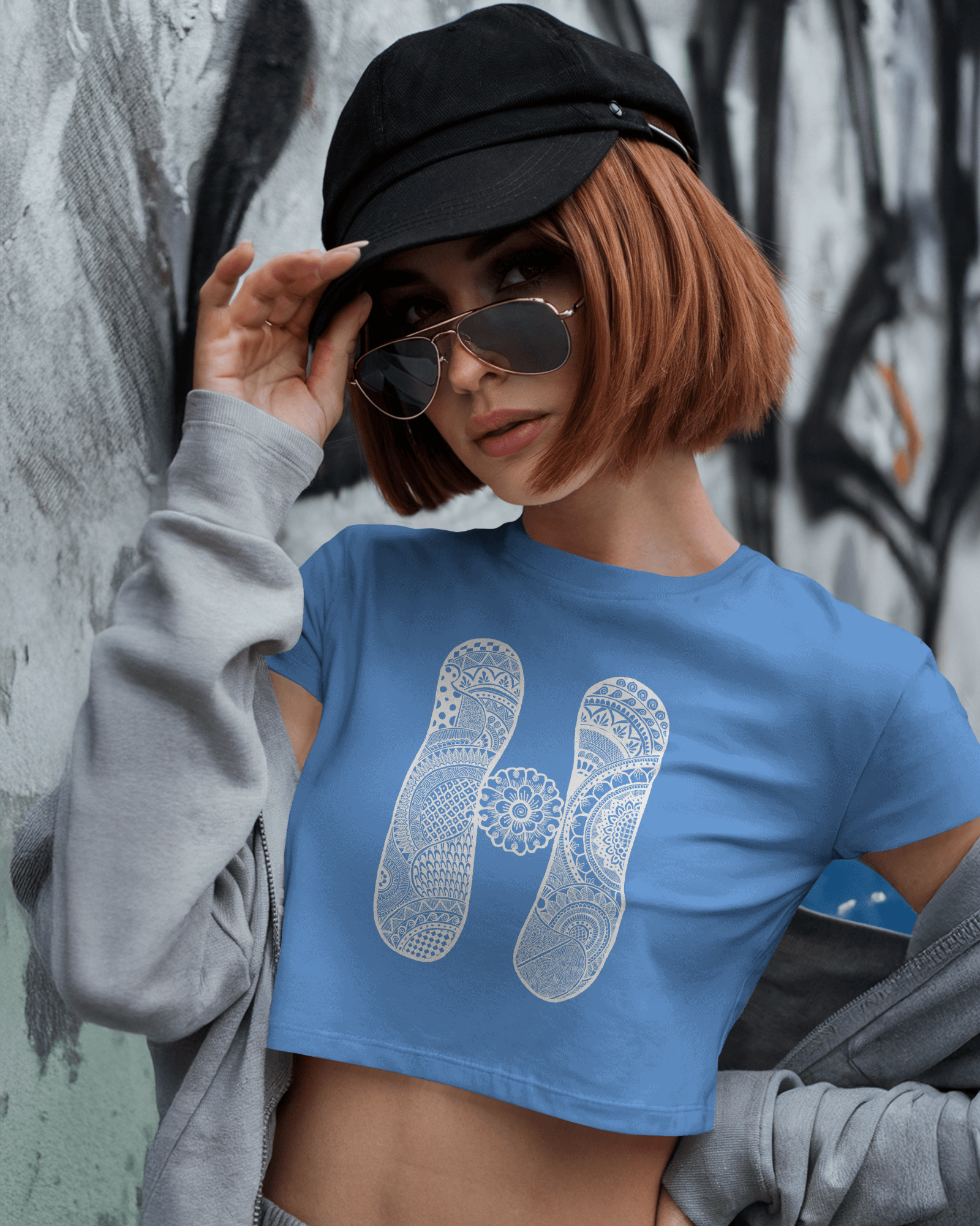 Person wearing a blue t-shirt with a white logo and a black cap, standing against a graffiti-covered wall.