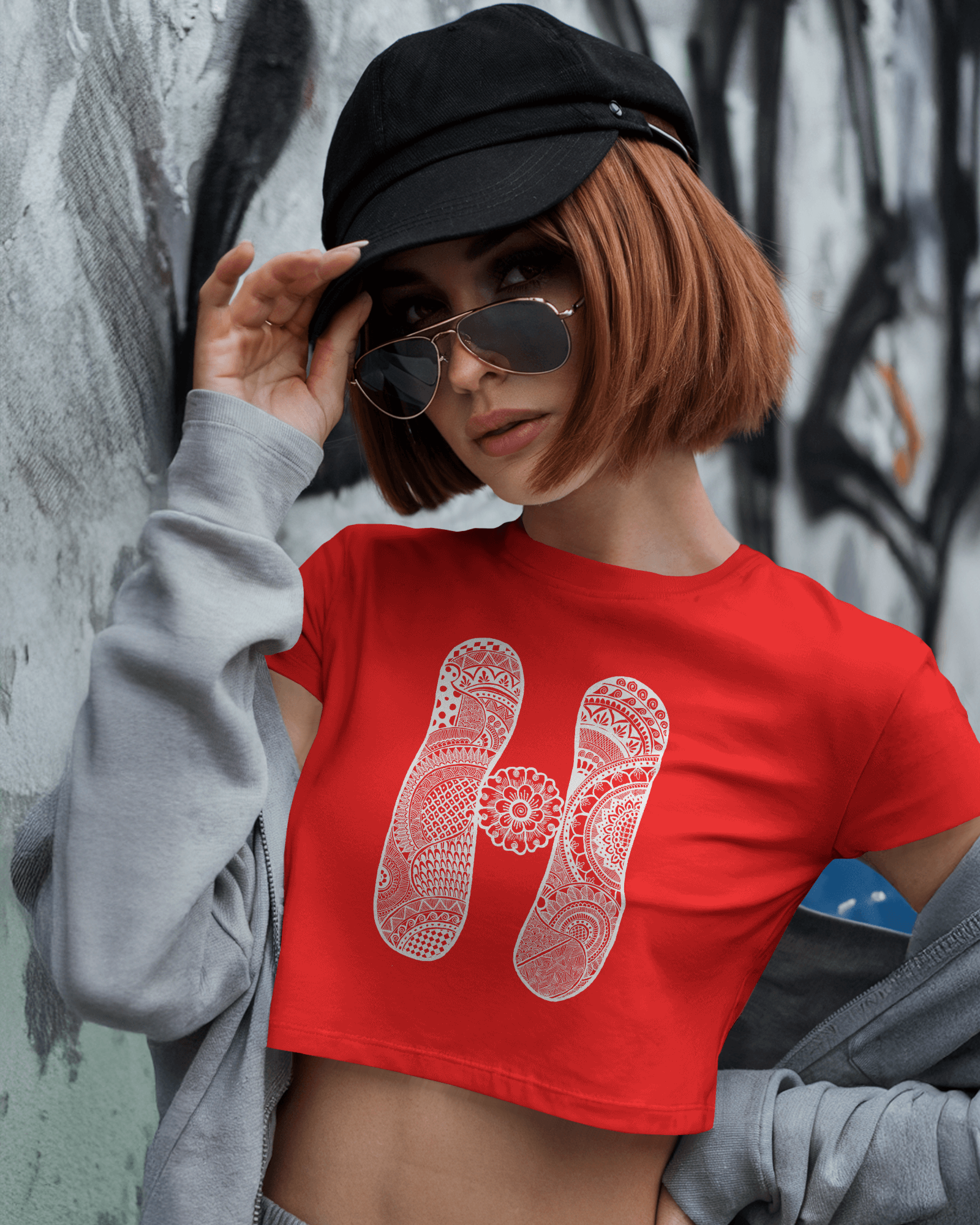 Person wearing a red t-shirt with a white logo, black cap, and sunglasses against a graffiti-covered wall.