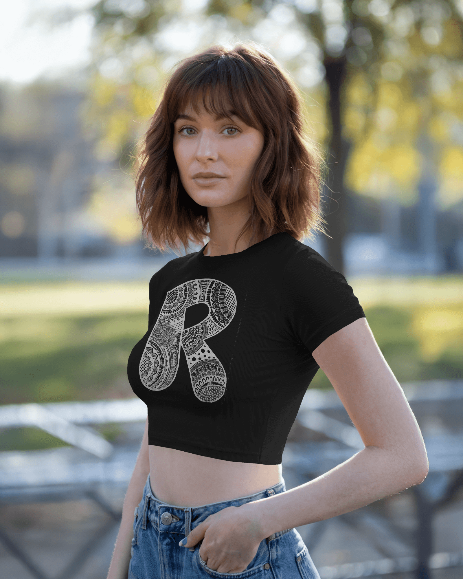 Woman wearing a black crop top with a decorative 'R' design outdoors.
