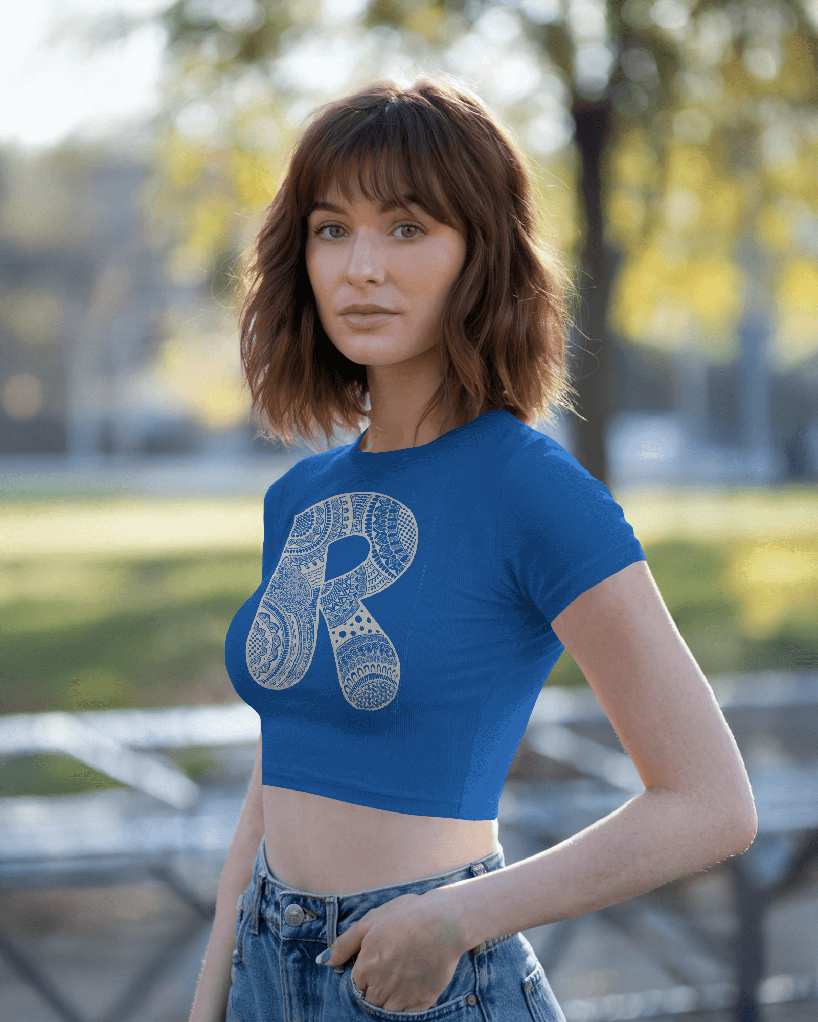 Woman wearing a blue crop top with a large letter 'R' design outdoors.