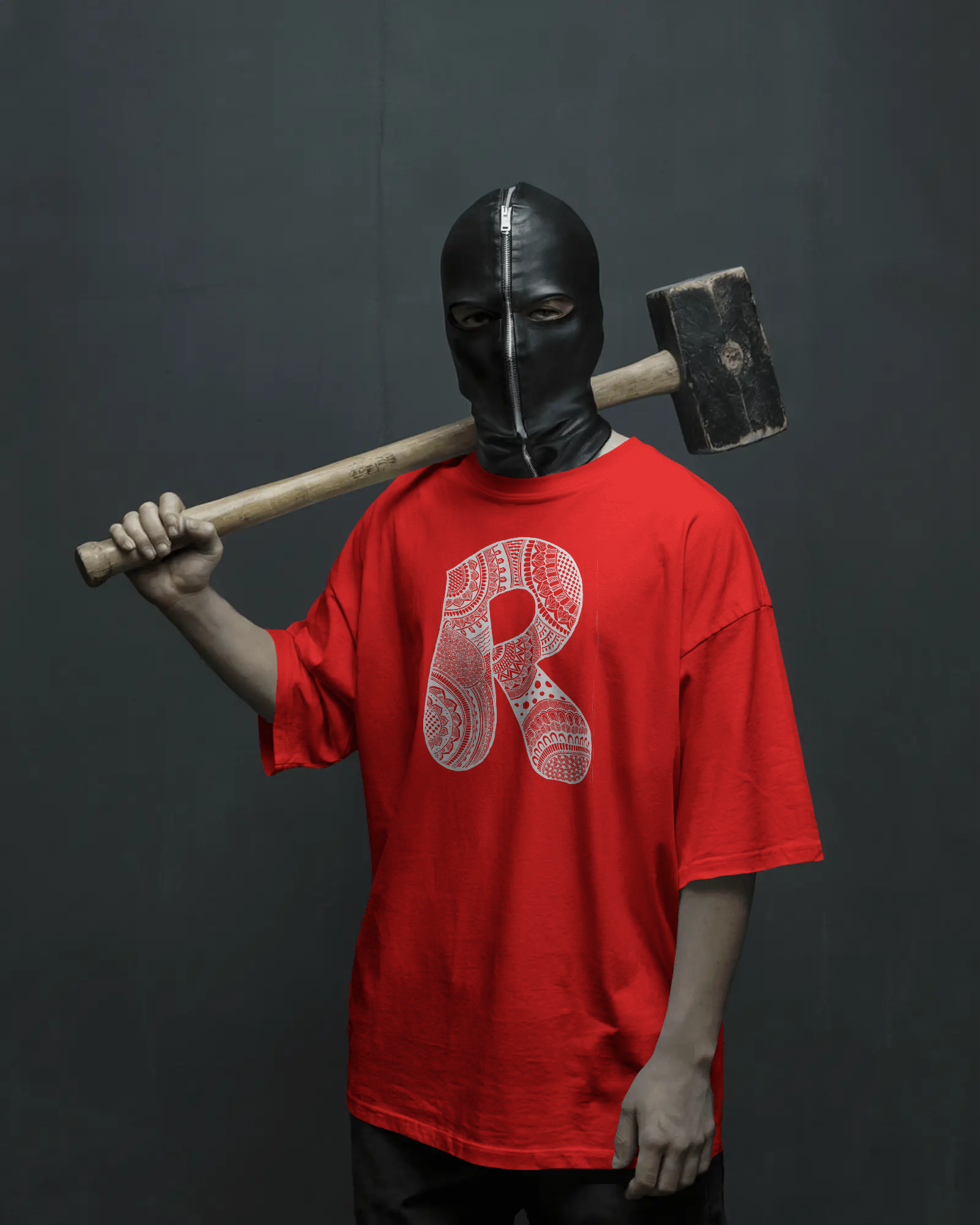 A woman wearing a black oversized T-shirt with a detailed white mandala letter R printed on the front, standing against a light neutral background.