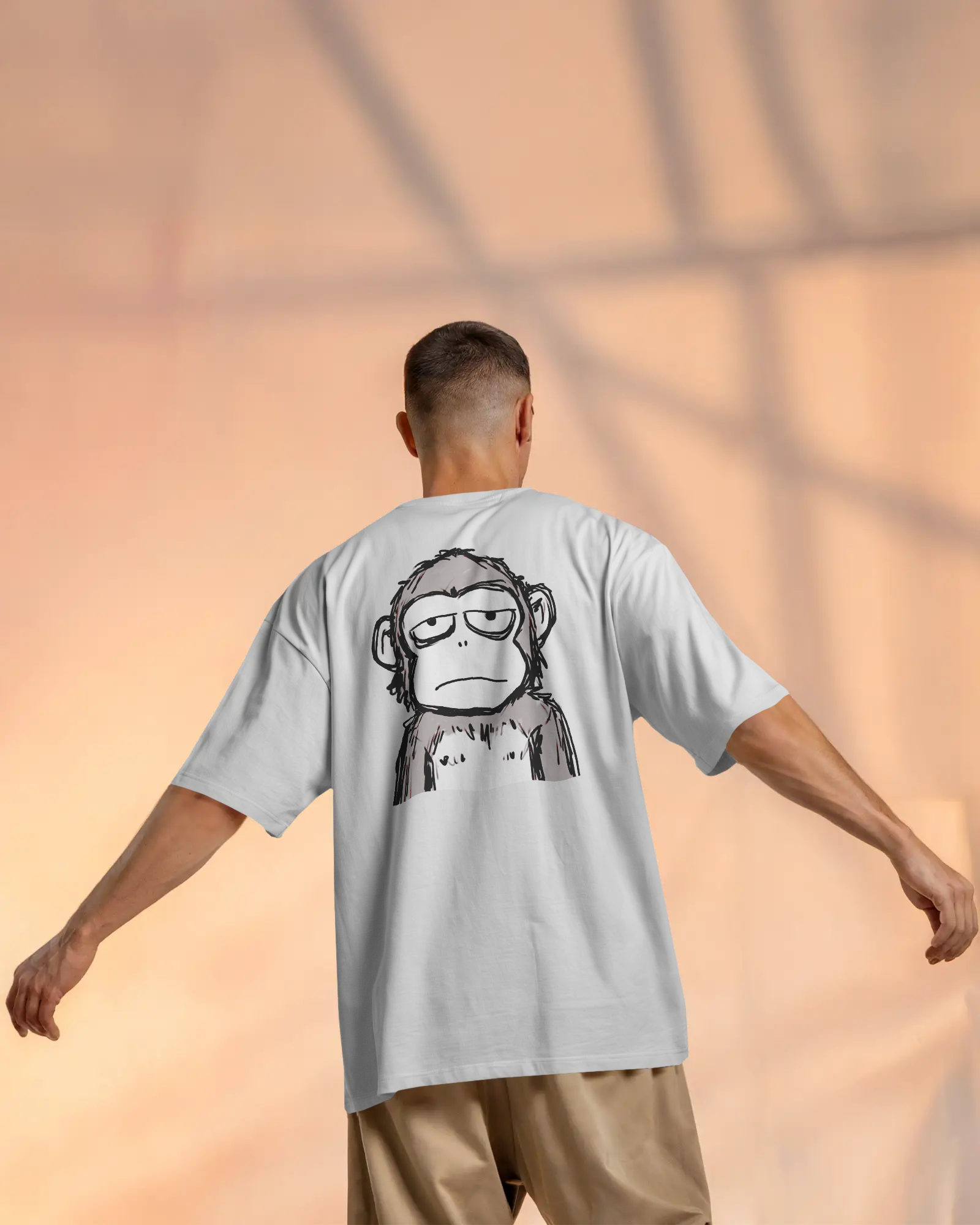 Person wearing a light gray t-shirt with a monkey graphic on the back, standing against a warm-toned background.